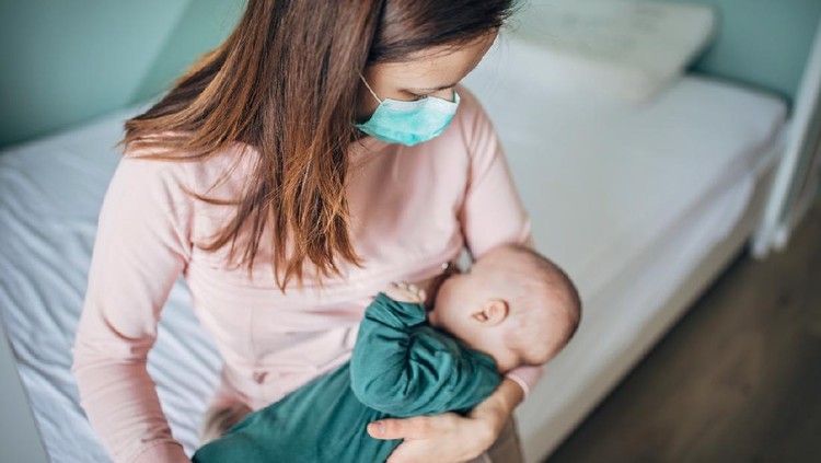 Two people, mother with protective mask breastfeeding her baby son at home, they are at home do to pandemic outbreak quarantine.