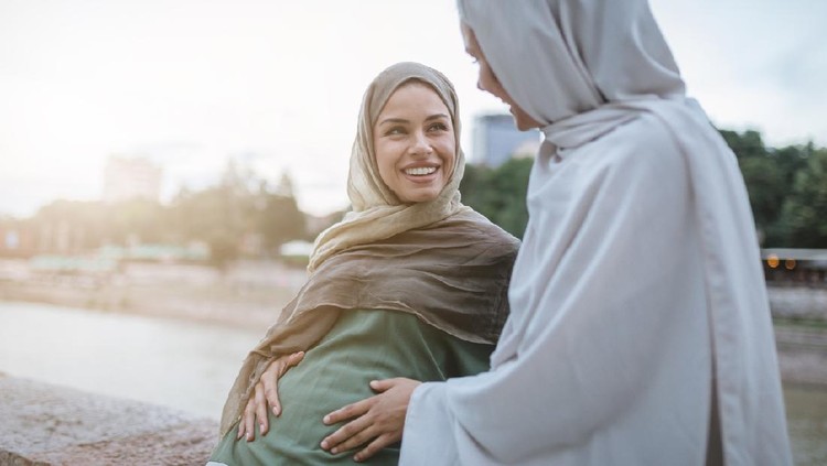 Cute and lovely pregnant Muslim woman and her Muslim friend, spending the time together on a city street.
