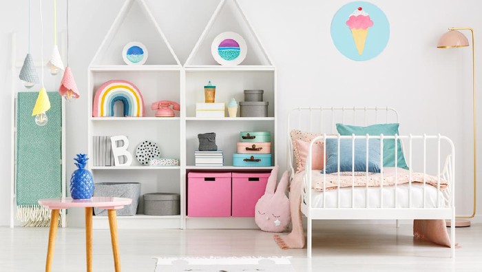 Front view of a kid's room with a table, shelves with boxes and rainbow, single bed and ice cream poster on the wall
