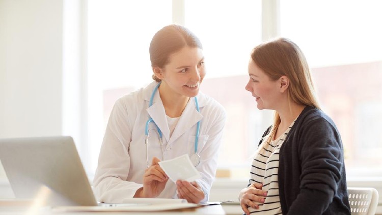 Portrait of female obstetrician smiling at pregnant woman in doctors office, copy space