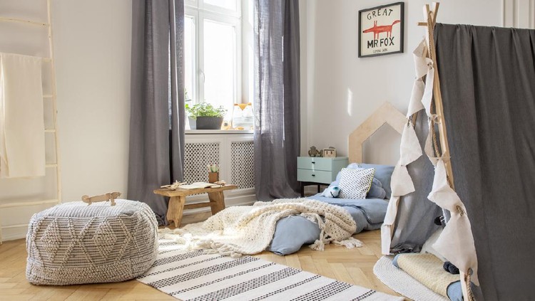 Pouf and tent in bright kid's bedroom interior with drapes at window and blanket on blue bed. Real photo