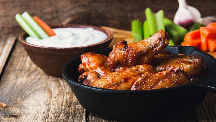 Roasted chicken wings with carrots, celery sticks and dipping sauce on rustic wooden table