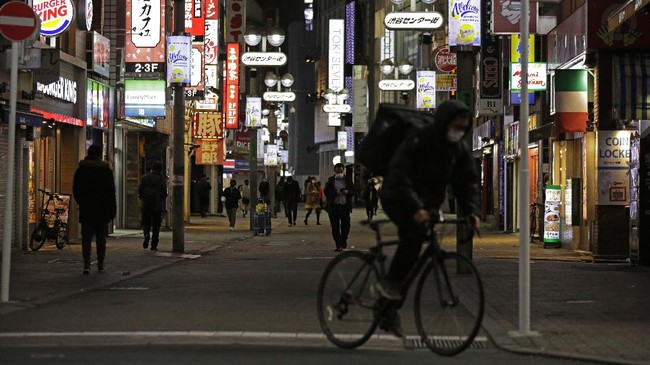 In this April 25, 2020, photo, people walk through the entertainment district near Shibuya station right before the 8pm government requested closing time for restaurants and bars in Tokyo. Under Japan's coronavirus state of emergency, people have been asked to stay home. Many are not. Some still have to commute to their jobs despite risks of infection, while others are dining out, picnicking in parks and crowding into grocery stores with scant regard for social distancing. (AP Photo/Kiichiro Sato)