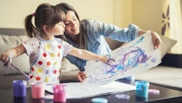 A young mother and her cute little daughter painting with colorful paints and having fun at home.