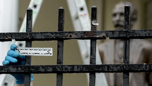 A statue of Cuban national hero Jose Marti is visible behind Secret Service investigators as they look at three bullet holes in a fence after police say a person with an assault rifle opened fire at the Cuban Embassy, Thursday, April 30, 2020, in Washington. (AP Photo/Andrew Harnik)