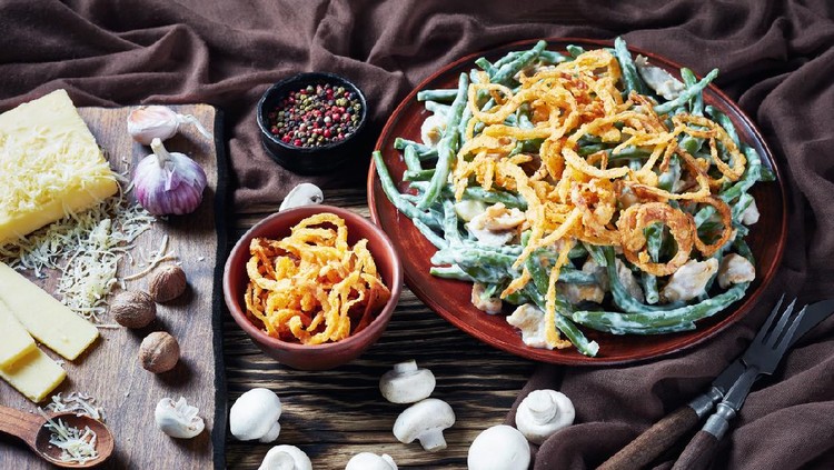 close-up of classic Green Bean Casserole served on an earthenware plate on  rustic wooden table with ingredients on a cutting board and brown cloth, american cuisine, view from above,