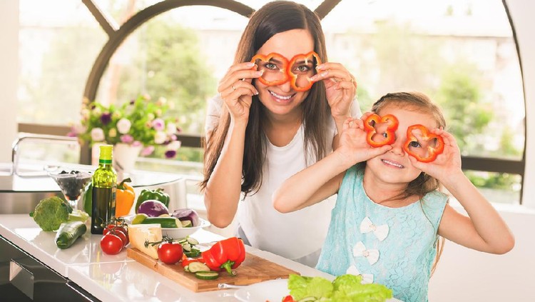 Happy family keeps fresh pieces of bell pepper. Cute little girl cooking with her mother. Cooking vegetarian meal at kitchen. Making salad. Healthy lifestyle. Recipe of vitamins nutrition
