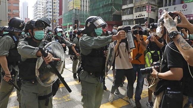 A riot police points the pepper spray to journalists as pro-democracy activists gather outside a shopping mall during the Labor Day in Hong Kong, Friday, May 1, 2020 amid an outbreak of the new coronavirus. May Day usually brings rallies and celebrations rallies marking international Labor Day. This year it's a bitter reminder of how much has been lost for the millions left idle or thrown out of work thanks to the coronavirus pandemic. (AP Photo/Kin Cheung)