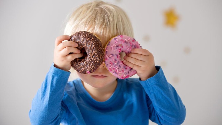 1202734638 Cute sweet blonde child, playing and eating donuts at home
