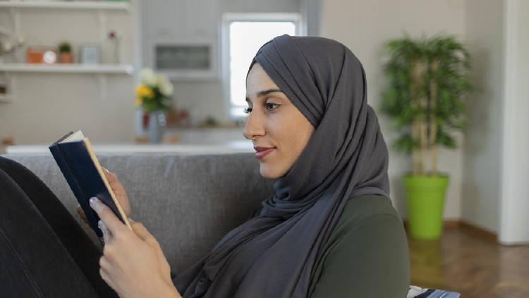 Beautiful Muslim Girl With Hijab Reading a Book While Sitting on the Sofa in the Living Room.