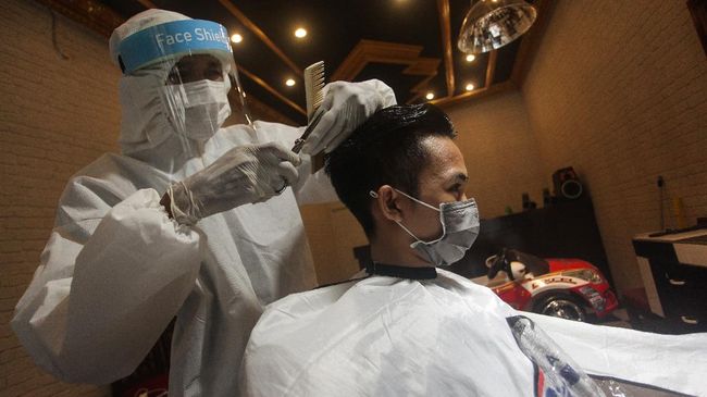 Seorang tukang pangkas rambut menggunakan alat pelindung diri (APD) saat mencukur rambut pelanggannya di Jalan Patih Rumbih, Palangkaraya, Kalimantan Tengah, Jumat (1/5/2020). Menurut pemilik salon, penggunaan APD tersebut sebagai antisipasi terhadap penyebaran COVID-19 serta membuat pelanggan merasa nyaman saat menggunakan jasanya. ANTARA FOTO/Makna Zaezar/wsj.