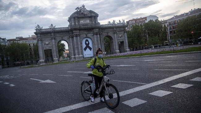 In this photo taken on Saturday, April 25, 2020, a woman rides Madrid's electric bike hire service BiciMAD in front of a Puerta de Alcala square with a black ribbon for the victims of COVID-19 as the lockdown to combat the spread of coronavirus continues in downtown Madrid, Spain. As countries seek to get economies back on track after the outbreak, bicycle use is being encouraged as a way to avoid any unsafe crowding on trains and buses. (AP Photo/Manu Fernandez)