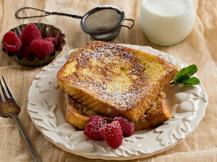A high angle close up shot of some french toast, raspberries and a glass of milk.