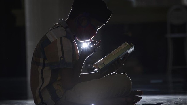 A child wears a face mask and reads the Koran during the Islamic holy month of Ramadan at a mosque in Darussalam, Banda Aceh on May 4, 2020. (Photo by CHAIDEER MAHYUDDIN / AFP)