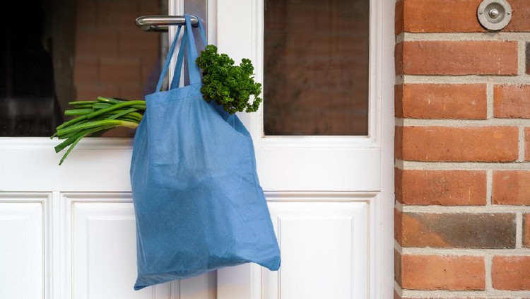 Blue shopping bag with fresh vegetables and goods was hanged on the front door, help concept during quarantine time because of coronavirus infection, copy space, selected focus
