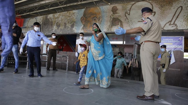 Railway and police officers gesture towards a migrant worker as she walks to board a special train to return to Agra in Uttar Pradesh state, during a nationwide lockdown to curb the spread of new coronavirus, at a railway station in Ahmedabad, in the western Indian state of Gujarat, Saturday, May 2, 2020. India on Friday ran the first train service for thousands of migrant workers desperate to return home since it imposed a nationwide lockdown to control the spread of the coronavirus. Several states, including Rajasthan, Jharkhand, Bihar, Kerala, Maharashtra, Uttar Pradesh, Punjab and Telangana have demanded special trains for returning workers because they couldn't arrange enough buses. Around 1 million migrant workers from Uttar Pradesh are still stranded in other Indian states, state government spokesman, Awanish Awasthi said. (AP Photo/Ajit Solanki)