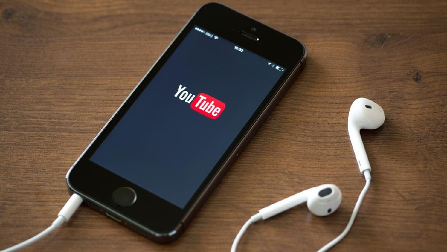 Kiev, Ukraine - June 5, 2014: Brand new Apple iPhone 5S with YouTube application service on the screen lying on a desk with headphones. YouTube is the world's most popular online video-sharing website that founded in February 14, 2005