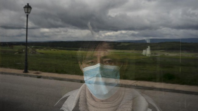 In this April 28, 2020 photo, Eusebio Soria poses for a photo behind a glass door at the entrance of his home as he recovers from the new coronavirus in Cabrejas del Pinar, Spain, in the province of Soria. Soria said that at first his doctor diagnosed him with the flu until his fever wouldn't go away and he was sent to the hospital where he spent 11 days after being tested positive for the coronavirus. Many in Spain's small and shrinking villages thought their low populations would protect them from the coronavirus pandemic. The opposite appears to have proved true. Soria, a north-central province that's one of the least densely peopled places in Europe, has recorded a shocking death rate. Provincial authorities calculate that at least 500 people have died since the start of the outbreak in April. (AP Photo/Felipe Dana)