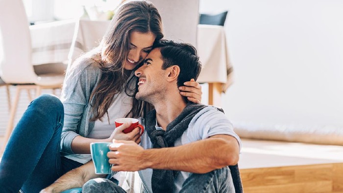 Happy couple in love sitting on the floor, embracing, smiling and drinking coffee, with copy space.