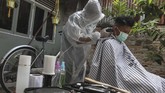 Jasa Pangkas Rambut Gunakan APD Seorang tukang cukur menggunakan Alat Pelindung Diri (APD) ketika memotong rambut di halaman rumah pelanggan, di Pekanbaru, Riau, Kamis (9/4/2020). Sepinya pengunjung yang datang ke barbershop membuat pelaku usaha potong rambut menerima jasa panggilan cukur ke rumah dengan menggunakan pakaian pelindung untuk pencegahan penularan virus Corona (COVID-19). ANTARA FOTO/Rony Muharrman/aww.