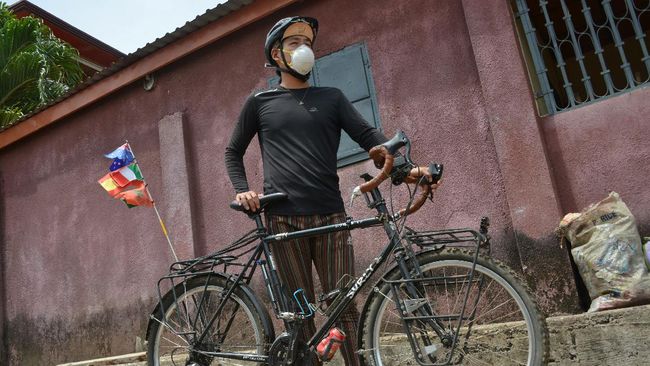 Cyclist Raymond Lee poses for a photograph while holding his bike on a street in Conakry, Guinea, on April 30, 2020. - Raymond Lee had been travelling the world by bicycle for two years when coronavirus struck and he found himself stranded in the poor West African state of Guinea. (Photo by CELLOU BINANI / AFP)