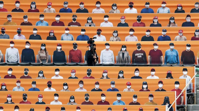 A TV cameraman walks through the spectators' seats which are covered with pictures of fans, before the start of a regular season baseball game between Hanwha Eagles and SK Wyverns in Incheon, South Korea, Tuesday, May 5, 2020. South Korea's professional baseball league start its new season on May 5, initially without fans, following a postponement over the coronavirus. (AP Photo/Lee Jin-man)