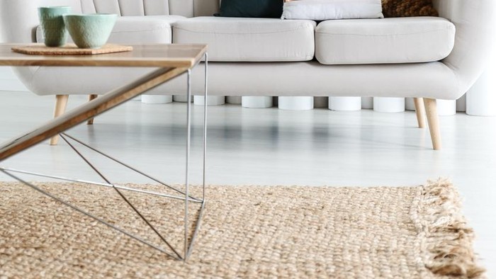 Designer table on brown carpet in front of grey sofa with decorative pillows against tubes in living room