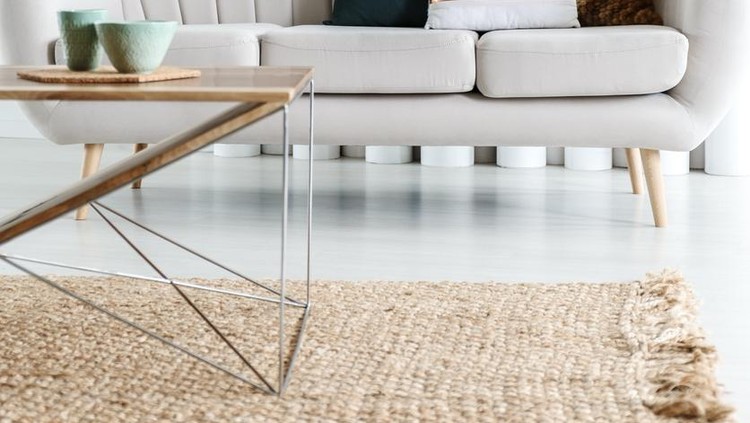 Designer table on brown carpet in front of grey sofa with decorative pillows against tubes in living room