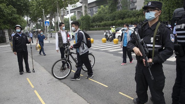 Police officers (R) stand guard at an entrance of a high school as senior students enter the premises in Wuhan in China's central Hubei province on May 6, 2020. - Senior school students returned to class on May 6 in the central Chinese city of Wuhan, where the coronavirus that has now swept the globe first emerged late last year. (Photo by STR / AFP) / China OUT