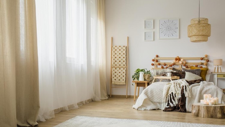 Candles on wood next to bed with knit blanket in hygge style bedroom interior with brown curtain and posters