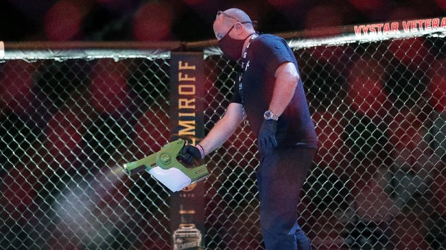 A worker sprays sanitizer in the octagon between bouts during a UFC 249 mixed martial arts competition, Saturday, May 9, 2020, in Jacksonville, Fla. (AP Photo/John Raoux)