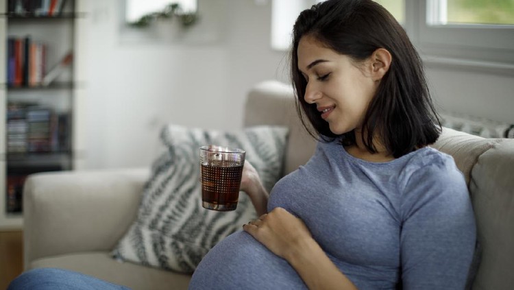 Pregnant woman sitting on her sofa drinking coffee and tea.