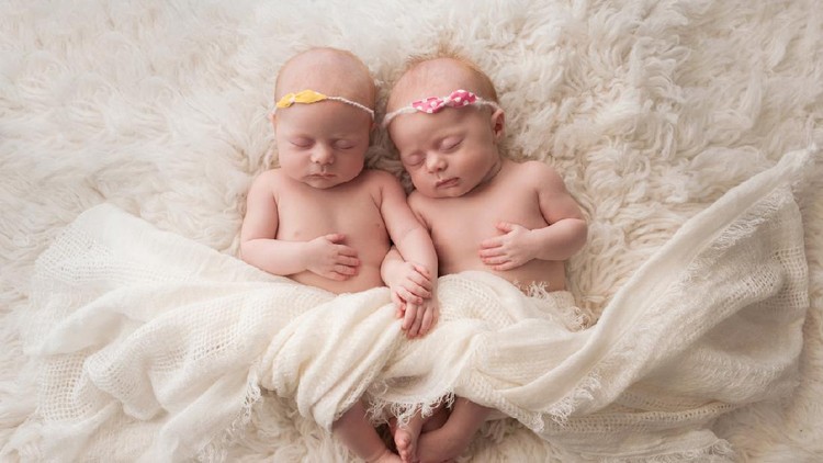 Seven week old fraternal, twin baby girls sleeping on a white flokati rug.