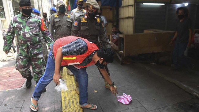 Seorang warga yang terjaring razia penindakan pelanggaran aturan Pembatasan Sosial Berskala Besar (PSBB) oleh Satpol PP menjalani hukuman dengan cara membersihkan sampah di Tanah Abang, Jakarta, Rabu (13/5/2020). Pemprov DKI Jakarta mulai memberlakukan sanksi sosial terhadap pelanggar PSBB yaitu dengan memakaikan rompi bertuliskan pelanggar PSBB saat mereka membersihkan fasilitas umum. ANTARA FOTO/Akbar Nugroho Gumay/aww.