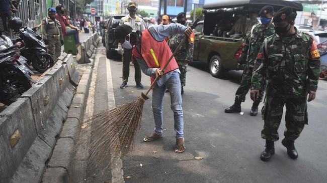 Seorang warga yang terjaring razia penindakan pelanggaran aturan Pembatasan Sosial Berskala Besar (PSBB) oleh Satpol PP menjalani hukuman dengan cara membersihkan sampah di Tanah Abang, Jakarta, Rabu (13/5/2020). Pemprov DKI Jakarta mulai memberlakukan sanksi sosial terhadap pelanggar PSBB yaitu dengan memakaikan rompi bertuliskan pelanggar PSBB saat mereka membersihkan fasilitas umum. ANTARA FOTO/Akbar Nugroho Gumay/aww.