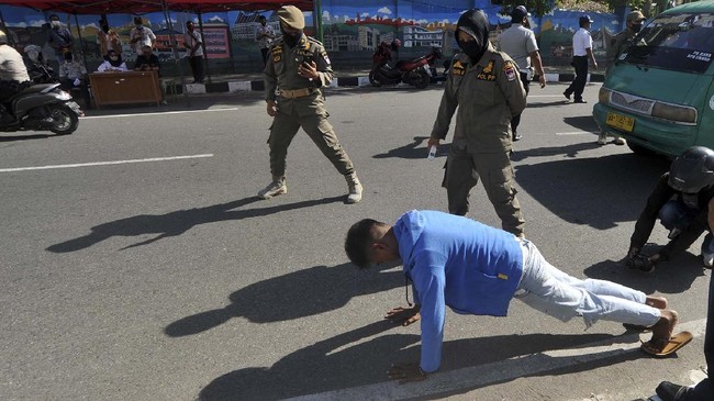 Petugas Satpol PP menghukum seorang pria dengan push up karena tidak menggunakan masker di Pasar Raya, Padang, Sumatera Barat, Jumat (15/5/2020). Pemkot Padang memperketat warga masuk ke Pasar Raya selama PSBB tahap kedua, dengan merazia masker dan pengecekan suhu tubuh karena pasar itu merupakan klaster terbanyak yang terdapat kasus positif COVID-19 di Padang. ANTARA FOTO/Iggoy el Fitra/pras.