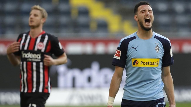 Frankfurt's Martin Hinteregger, left, runs past as Moenchengladbach's Ramy Bensebaini celebrates after scoring his sides third goal during the German Bundesliga soccer match between Eintracht Frankfurt and Borussia Moenchengladbach in Frankfurt, Germany, Saturday, March 16, 2020. The German Bundesliga becomes the world's first major soccer league to resume after a two-month suspension because of the coronavirus pandemic. (AP Photo/Michael Probst, Pool)