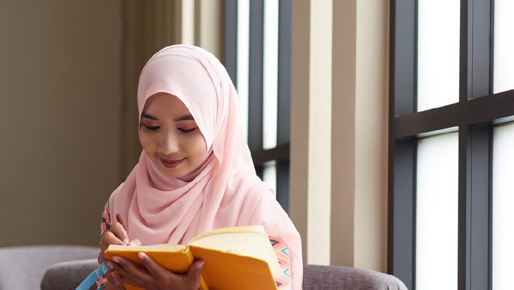 Muslim concept. Young muslim woman writing notebook paper, relaxing and enjoying her book.