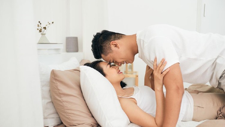 couple Side view of excited man is lying over woman in bed. They are looking at each other eyes and laughing