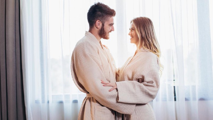 couple Side view of excited man is lying over woman in bed. They are looking at each other eyes and laughing