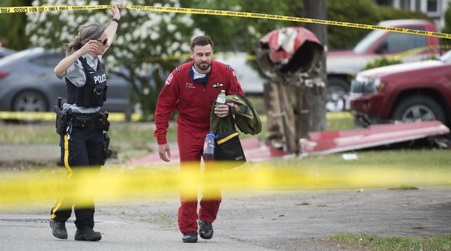 The remains of a downed Canadian Forces Snowbird plane is pictured as a member of the Snowbirds walks past in Kamloops, Canada, Sunday, May 17, 2020. The Canadian acrobatic jet crashed into the British Columbia neighborhood Sunday during a flyover intended to boost morale during the pandemic, killing at least one crew member, seriously injuring another and setting a house on fire. (Jonathan Hayward/The Canadian Press via AP)