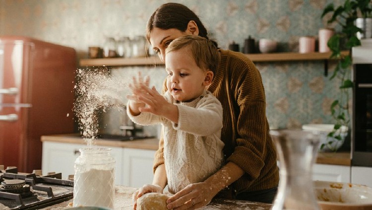 1137073322 Mother and son are preparing dough for cookies together in the morning. Kid is throwing flour and is happy.