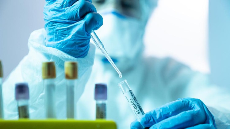 Close up photo of female scientist holding a laboratory pipette and a blood sample tube for covid-19 in laboratory. She is wearing a protective suit, laboratory glasses, surgical mask and surgical gloves. Selective focus on tube. Shot with a full frame mirrorless camera.
