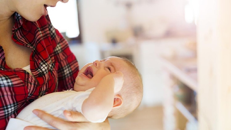 Bayi Rewel Crying little baby in the arms of her mother in a living room.