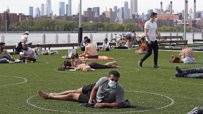 People relax in designated circles marked on the grass at Brooklyn's Domino Park during the current coronavirus outbreak, Monday, May 18, 2020, in New York. The circles were added after the park became severely overcrowded duirng a spate of uneasonably warm weather just over a week ago. (AP Photo/Kathy Willens)