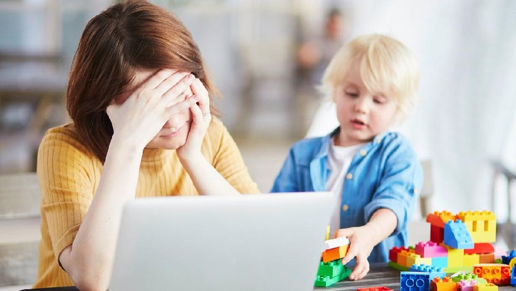 Boy playing near his tired mother working on her laptop. Quarantine and closed schools and offices during coronavirus outbreak. Homeschooling, distance learning and freelance job