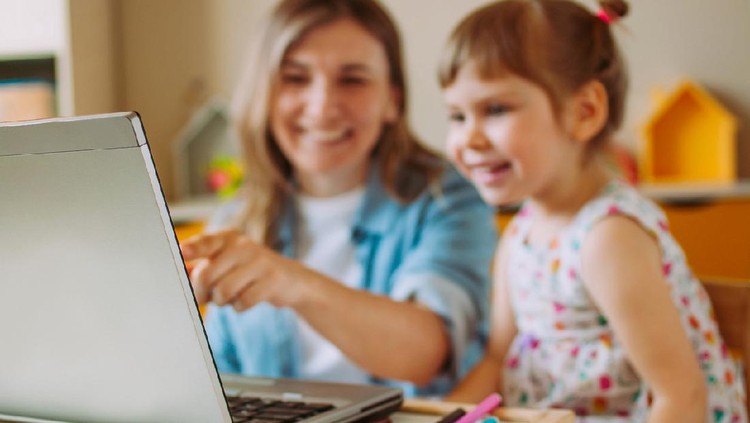 1217139876 Smiling mother and toddler daughter looking at the notebook indoor. Distance online learning concept. Activities for kids during quarantine. Focus on the notebook.
