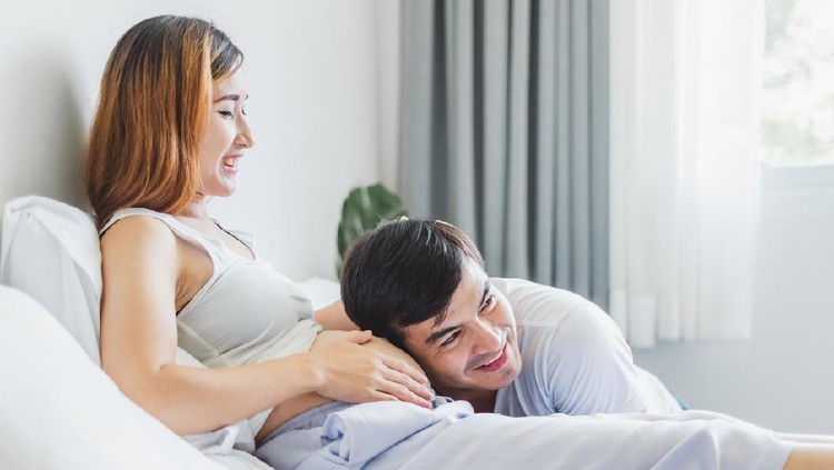 Young Asian husband touching/listening on belly pregnant wife with love and happy