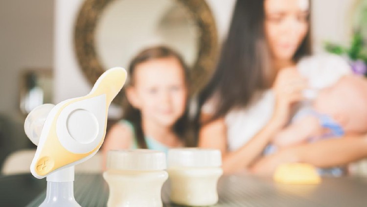 Bottle with milk and manual breast pump. Daughter holding baby bottle and helps to mother at background, kitchen. Mother's breast milk is the most healthy food for newborn baby. Happy family concept