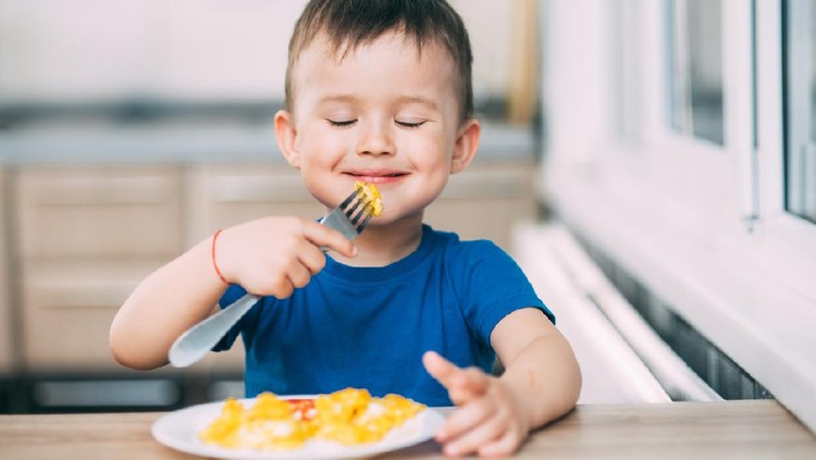 a child in a t-shirt in the kitchen eating an omelet, fork yourself